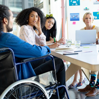 A diverse team including a wheelchair user collaborating around a meeting table in a bright office.